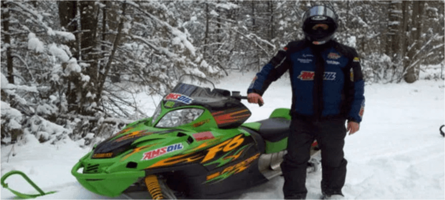 Dave Mann standing next to a green Arctic Cat snowmobile in winter