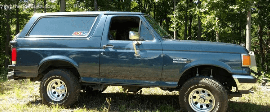 Blue Ford Bronco parked on a wooded property
