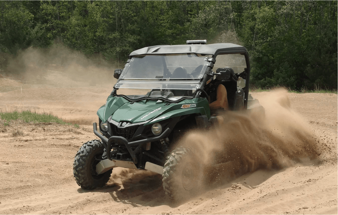 Green Yamaha Wolverine UTV kicking up dirt on a trail