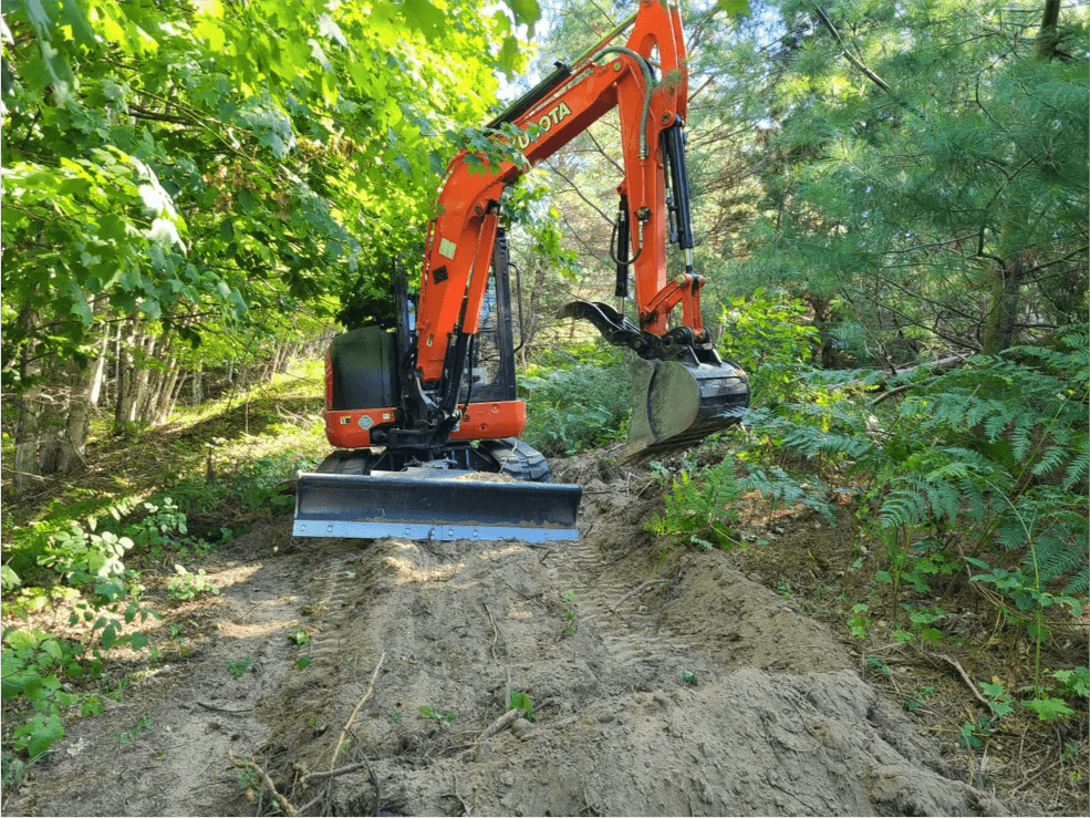 Orange Kubota mini excavator clearing a trail