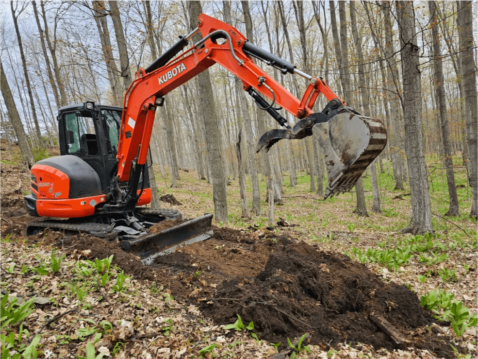 Orange Kubota mini excavator digging in the woods