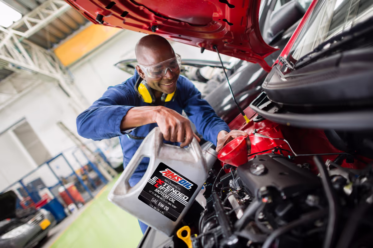 Technician pouring AMSOIL motor oil into a car engine at a service shop